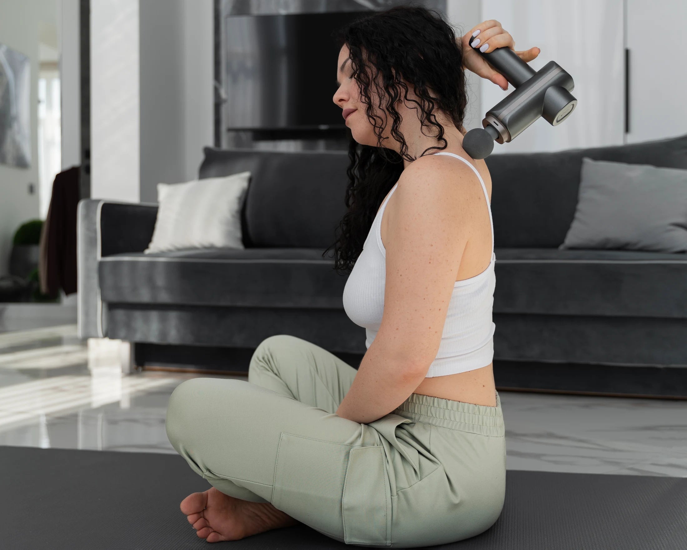 Woman using a massage gun to reach upper back and shoulder muscles